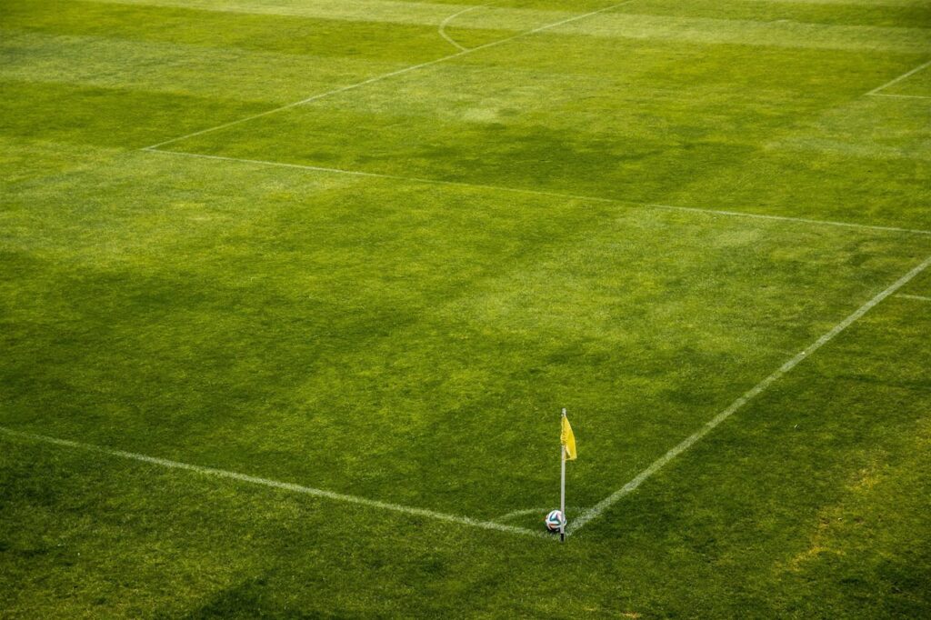 A vibrant green soccer field corner with a yellow flag and soccer ball, perfect for sports themes.